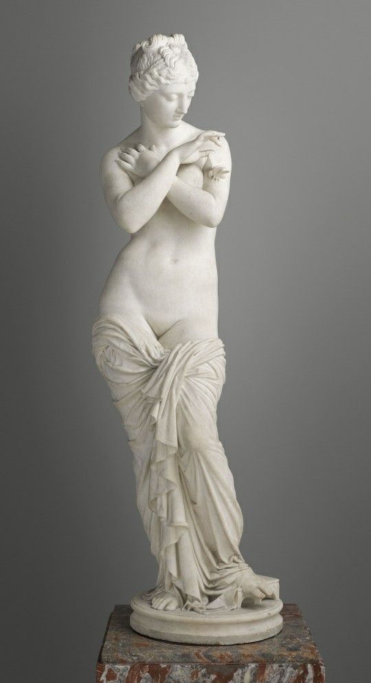 A white marble statue of a woman in a classical pose, partially draped, with arms crossed over her chest and a serene expression.
