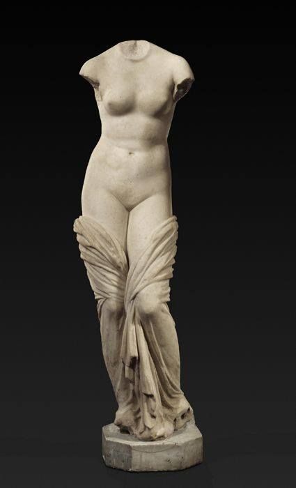 A classical marble statue of a female figure, missing its head and arms, draped in flowing fabric that accentuates the form of the body.